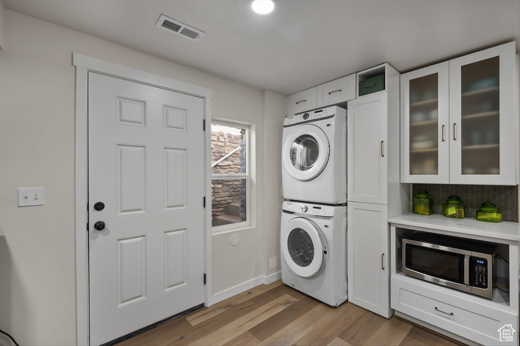 Washroom with visible vents, baseboards, light wood-type flooring, laundry area, and stacked washer / drying machine