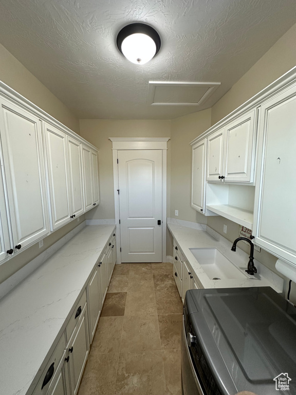 Laundry area with a sink, cabinet space, attic access, and a textured ceiling