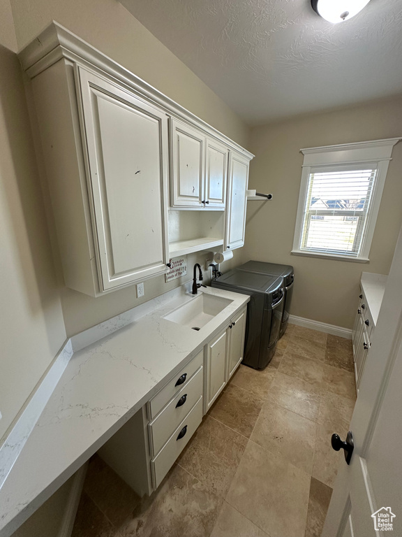 Washroom with a textured ceiling, a sink, washer and dryer, baseboards, and cabinet space