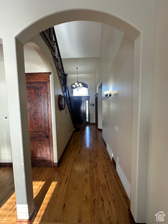 Hallway with wood-type flooring, baseboards, arched walkways, and stairs