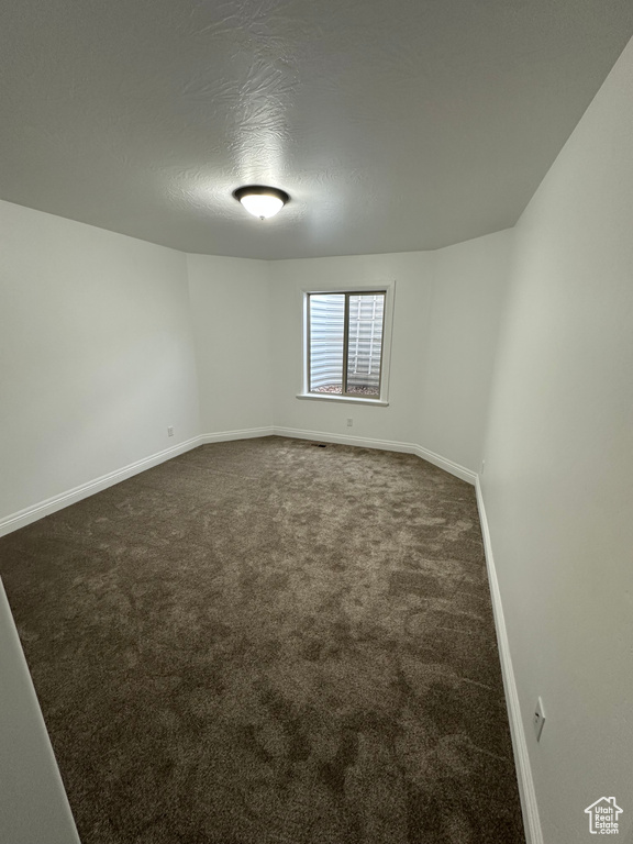 Empty room with baseboards, dark colored carpet, and a textured ceiling