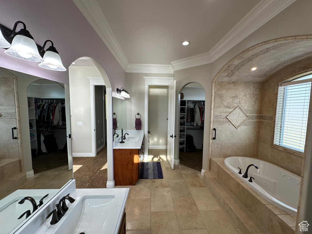 Bathroom with two vanities, crown molding, a walk in closet, a sink, and a tub with jets