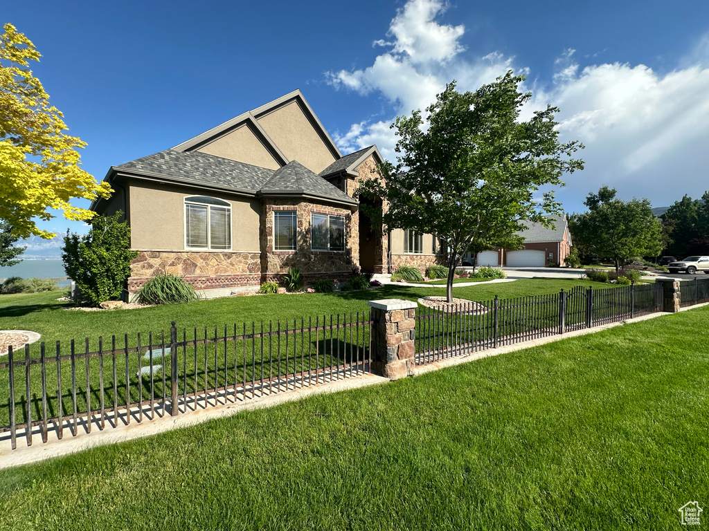 View of front of property featuring a fenced front yard, a front lawn, stone siding, and stucco siding