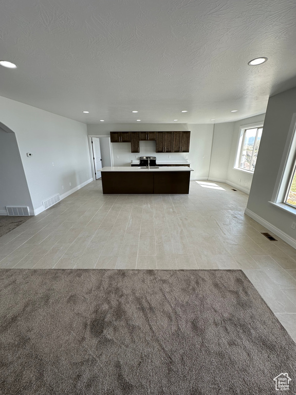 Kitchen with open floor plan, light carpet, visible vents, and dark brown cabinetry