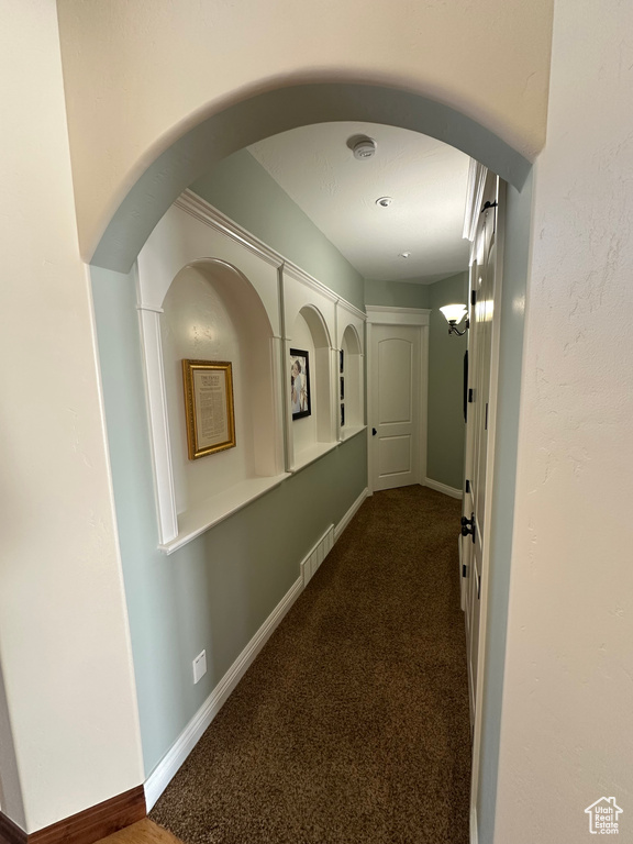 Hallway featuring arched walkways, carpet, visible vents, and baseboards