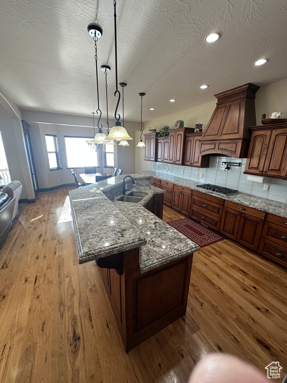 Kitchen featuring custom exhaust hood, backsplash, stainless steel gas cooktop, hardwood / wood-style flooring, and a sink