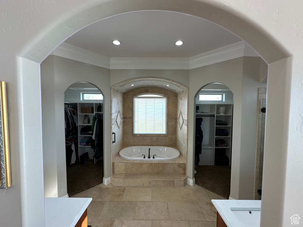 Full bath with a spacious closet, a garden tub, vanity, and ornamental molding
