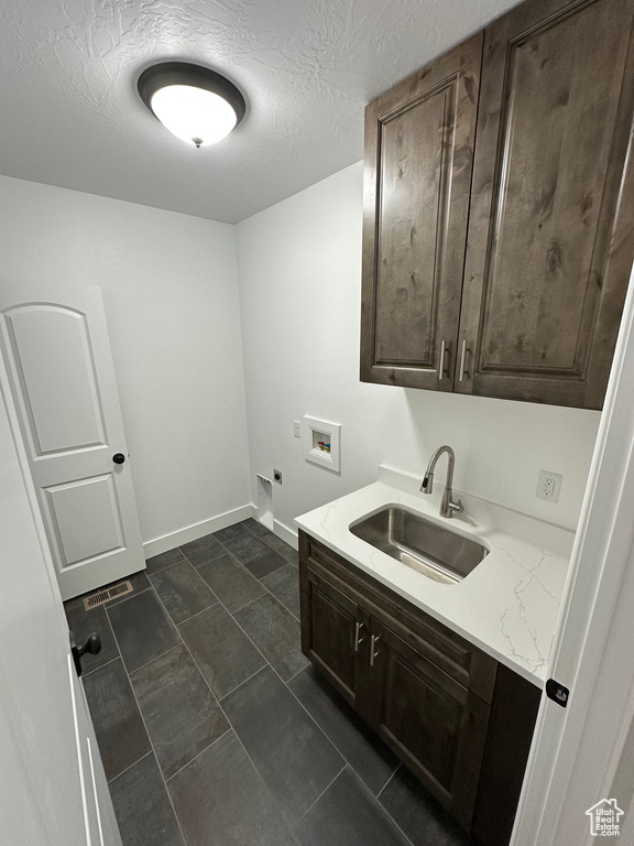 Clothes washing area featuring hookup for a washing machine, a textured ceiling, hookup for an electric dryer, a sink, and cabinet space