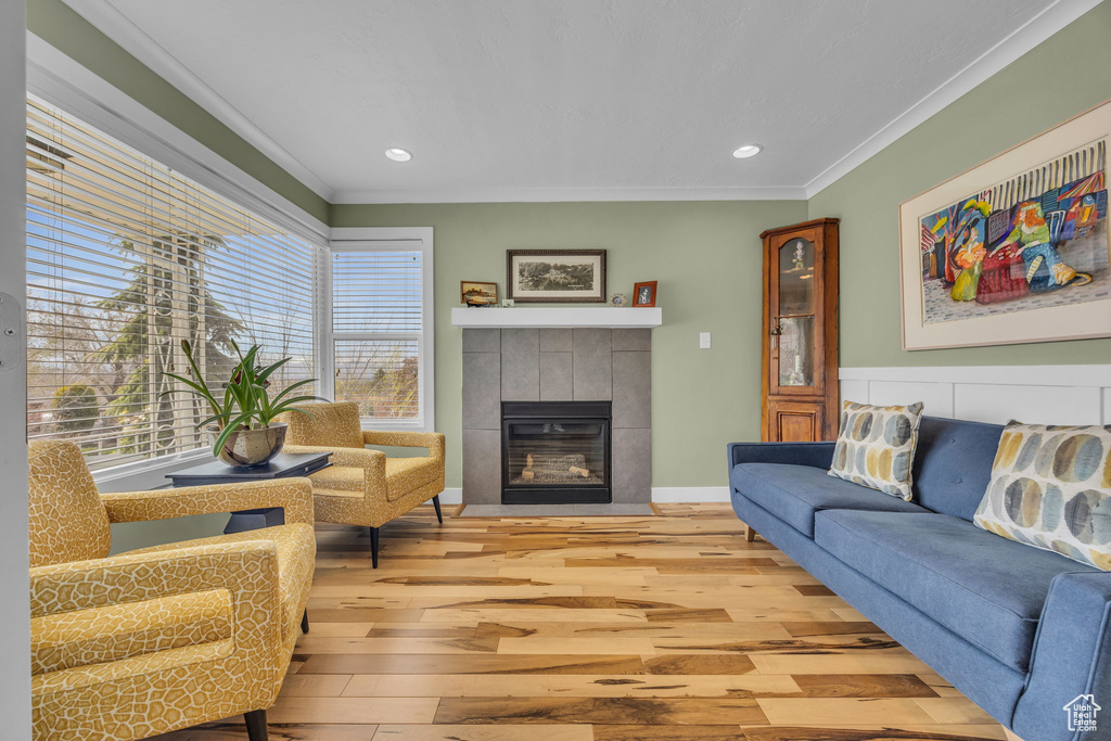 Living room with crown molding, light wood finished floors, a tiled fireplace, and recessed lighting