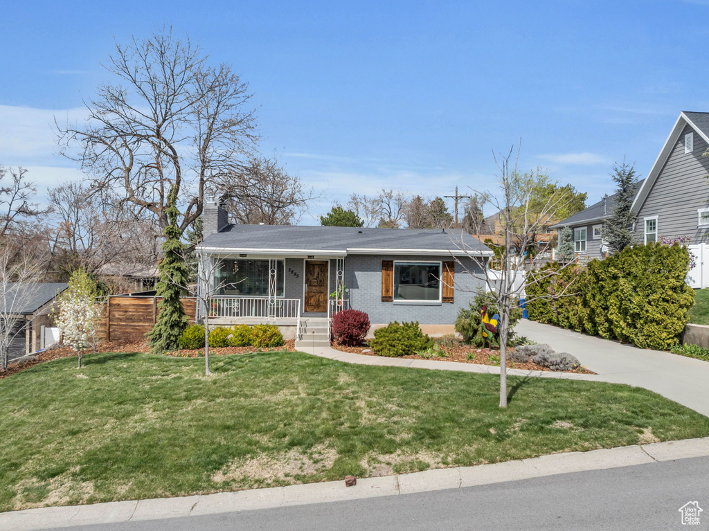 Ranch-style house featuring a front yard, a porch, a chimney, brick siding, and driveway
