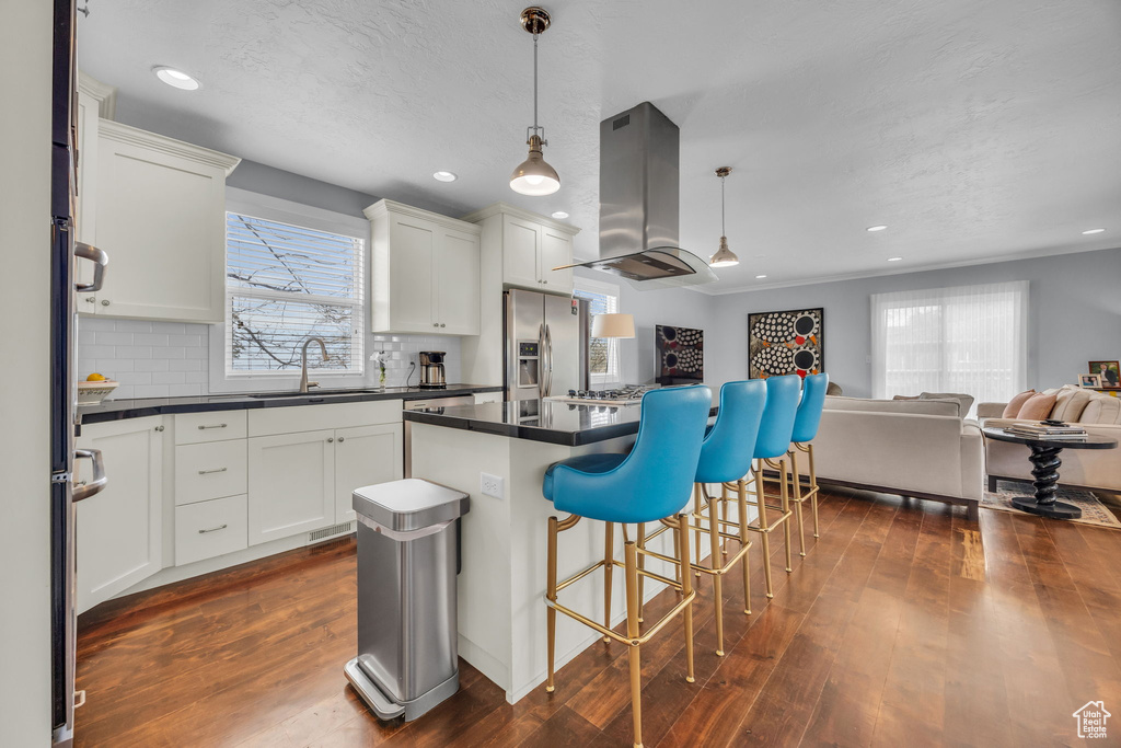Kitchen featuring stainless steel fridge with ice dispenser, a sink, open floor plan, dark countertops, and island range hood