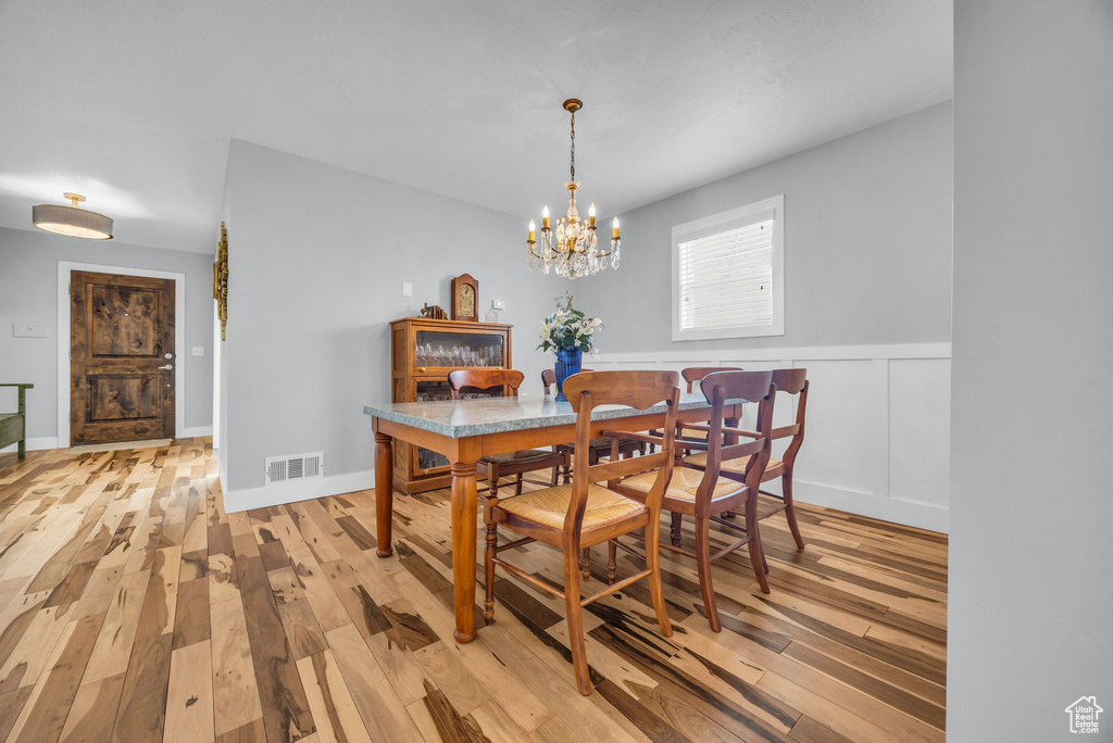 Dining area with light wood-style floors, a notable chandelier, visible vents, and a wainscoted wall