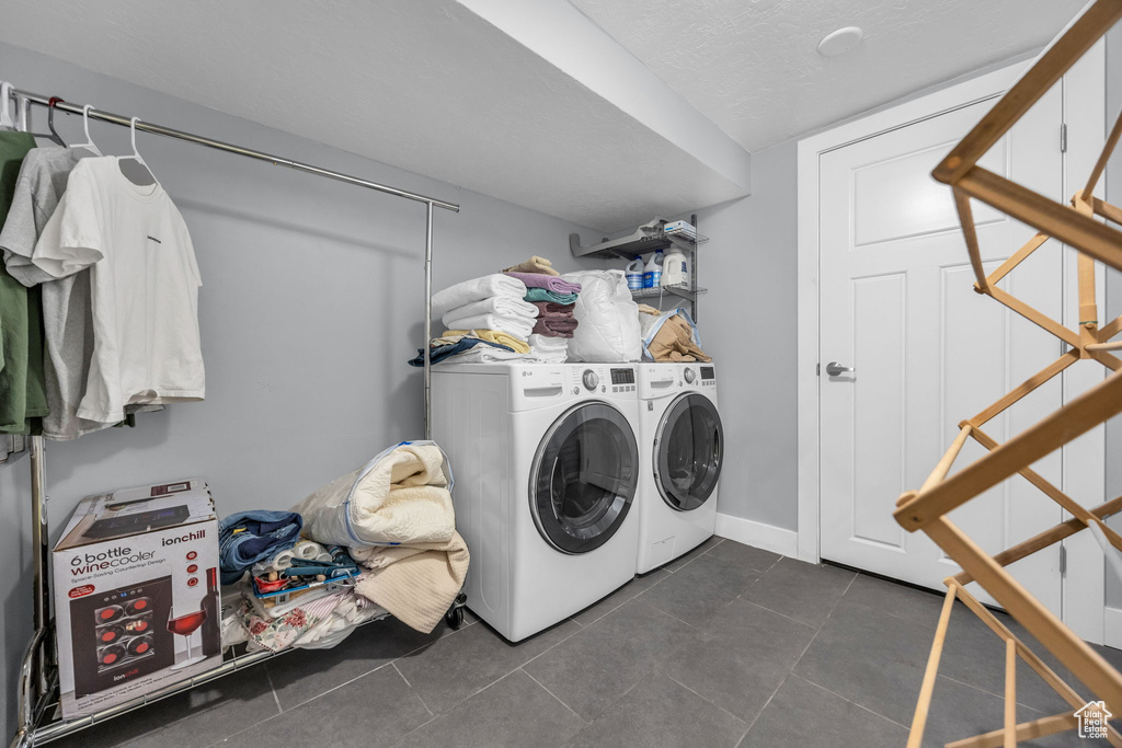 Laundry area with baseboards, a textured ceiling, laundry area, washing machine and clothes dryer, and dark tile patterned flooring