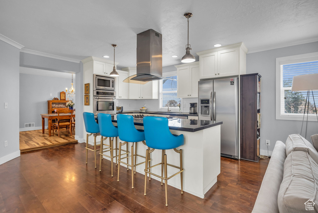 Kitchen with island exhaust hood, a center island, dark countertops, visible vents, and appliances with stainless steel finishes
