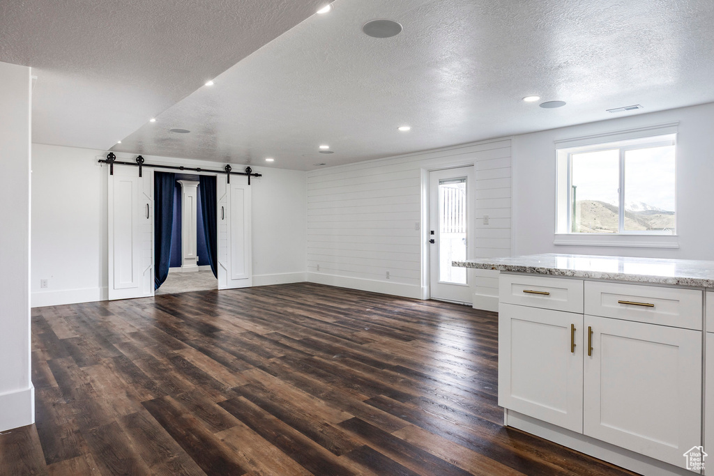 Unfurnished living room with a barn door, a textured ceiling, dark wood finished floors, and recessed lighting