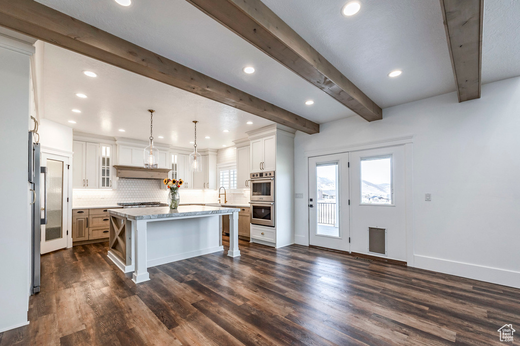 Kitchen with stainless steel appliances, decorative backsplash, beamed ceiling, a kitchen island, and dark wood-style flooring