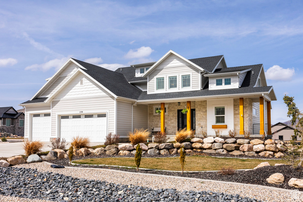 View of front facade featuring a porch, a garage, driveway, roof with shingles, and stone siding
