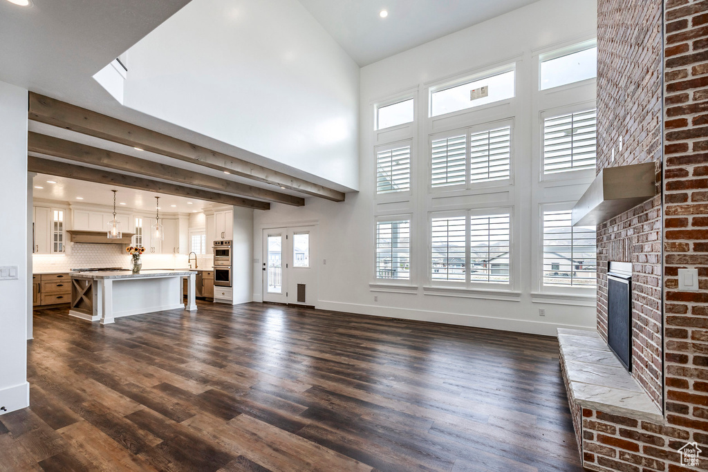 Unfurnished living room with a brick fireplace, a towering ceiling, dark wood-type flooring, and recessed lighting