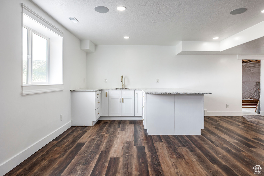 Kitchen featuring dark wood-style flooring, light stone counters, a peninsula, recessed lighting, and a textured ceiling