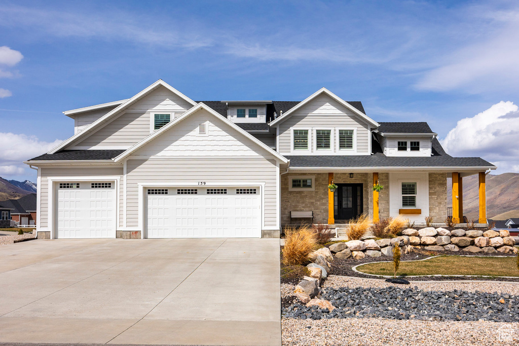 View of front of home featuring a porch, stone siding, concrete driveway, and an attached garage