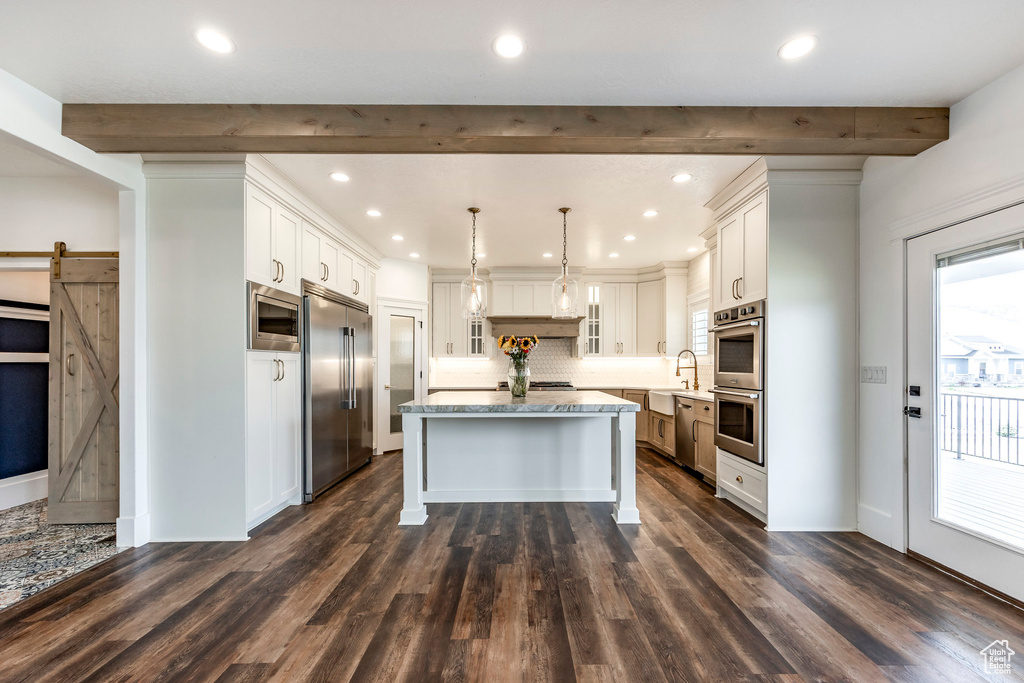 Kitchen with built in appliances, a barn door, a center island, backsplash, and dark wood-style flooring
