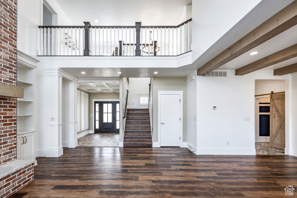 Unfurnished living room featuring a barn door, wood finished floors, stairway, recessed lighting, and a high ceiling