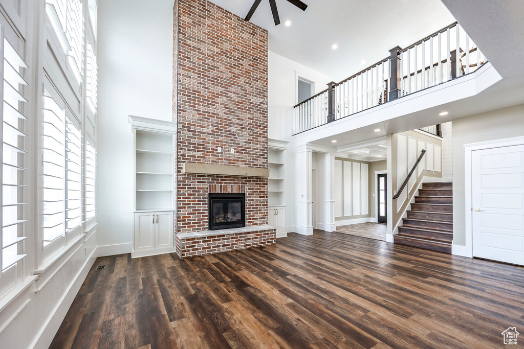 Unfurnished living room featuring a high ceiling, dark wood-style floors, a fireplace, stairway, and ceiling fan