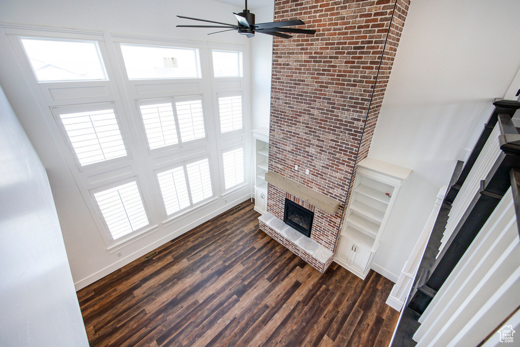 Unfurnished living room with a fireplace, a ceiling fan, and dark wood-style flooring