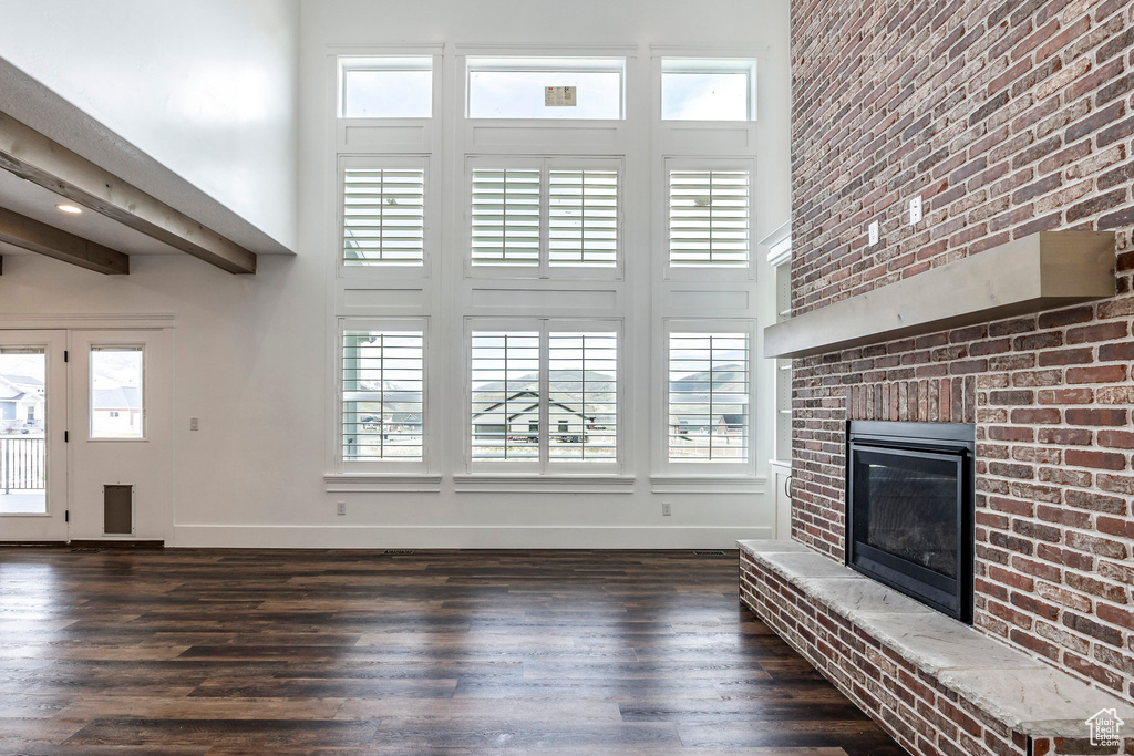 Unfurnished living room with a high ceiling, dark wood-style floors, and a brick fireplace