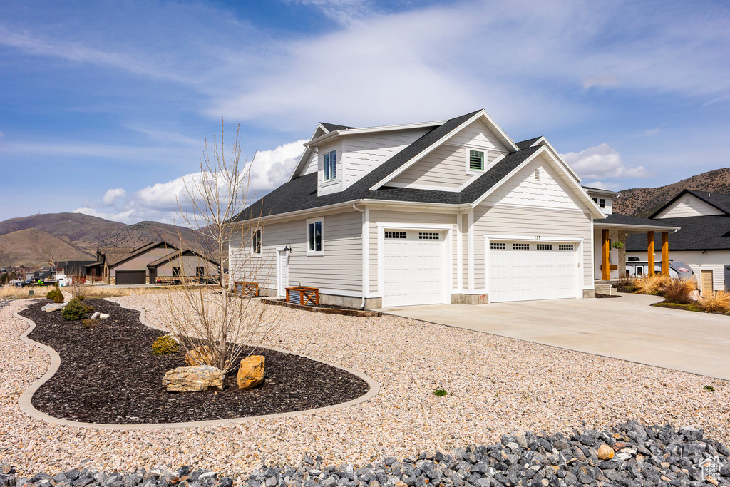 View of property exterior featuring a mountain view, concrete driveway, roof with shingles, and an attached garage