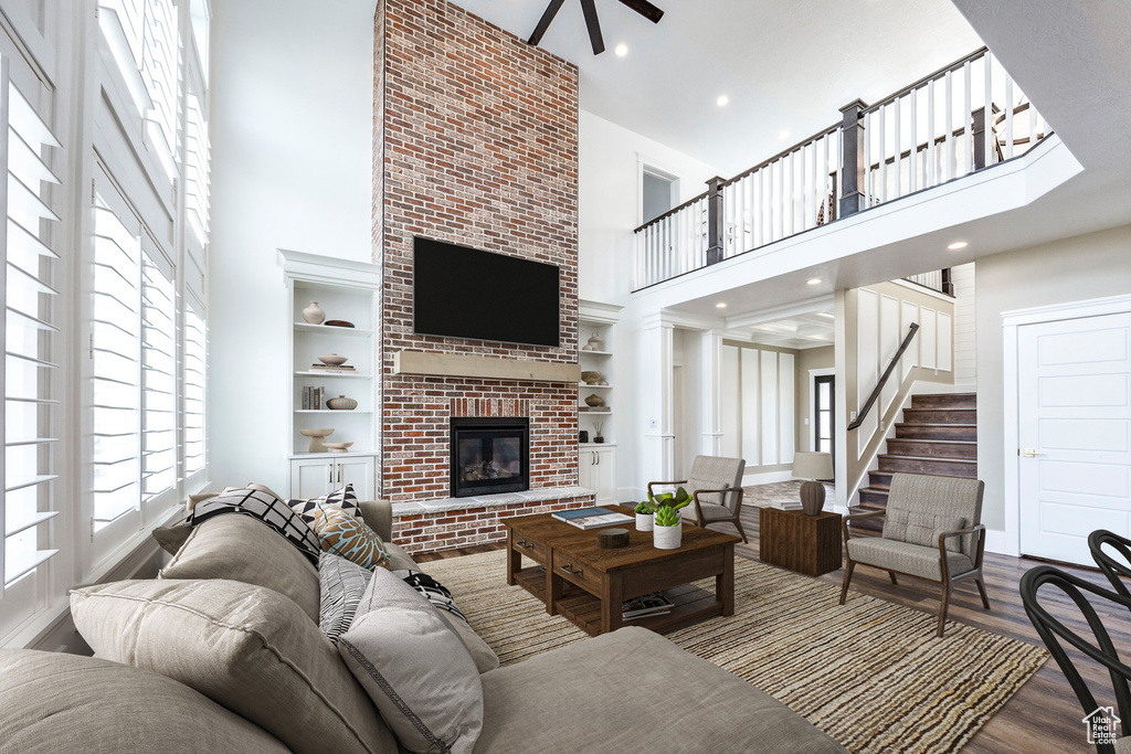 Living room with a towering ceiling, a brick fireplace, ceiling fan, wood finished floors, and built in features