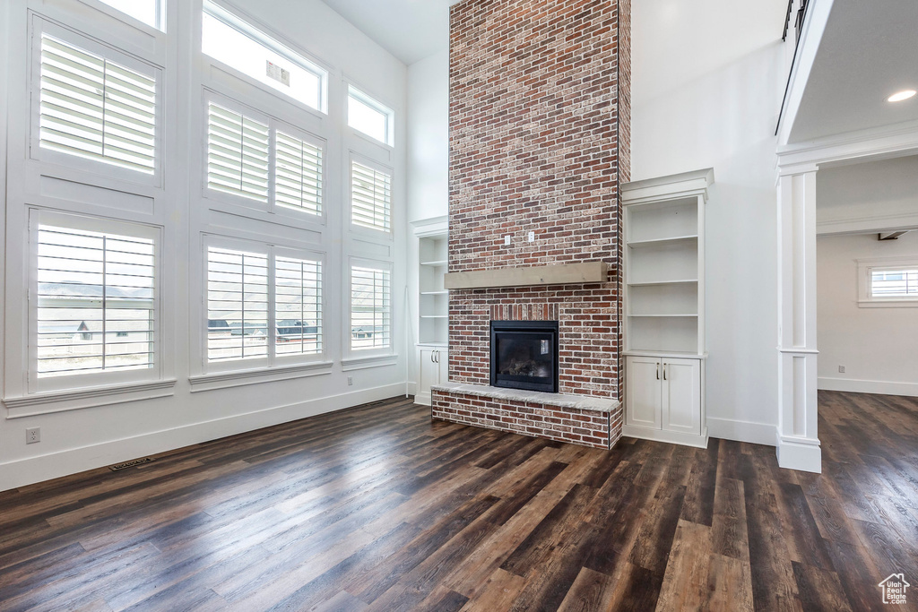 Unfurnished living room featuring a towering ceiling, dark wood finished floors, a brick fireplace, and ornate columns