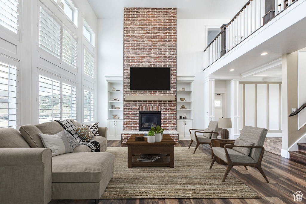 Living room featuring a towering ceiling, a brick fireplace, dark wood finished floors, built in shelves, and stairs