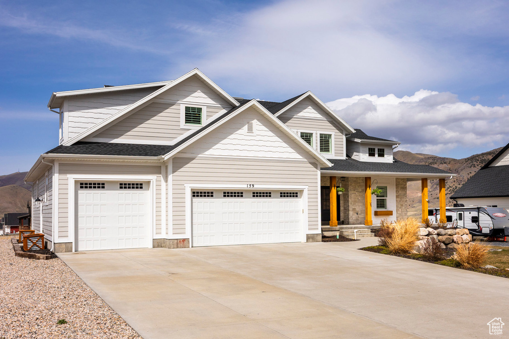 View of front of house with covered porch, driveway, a garage, a mountain view, and stone siding