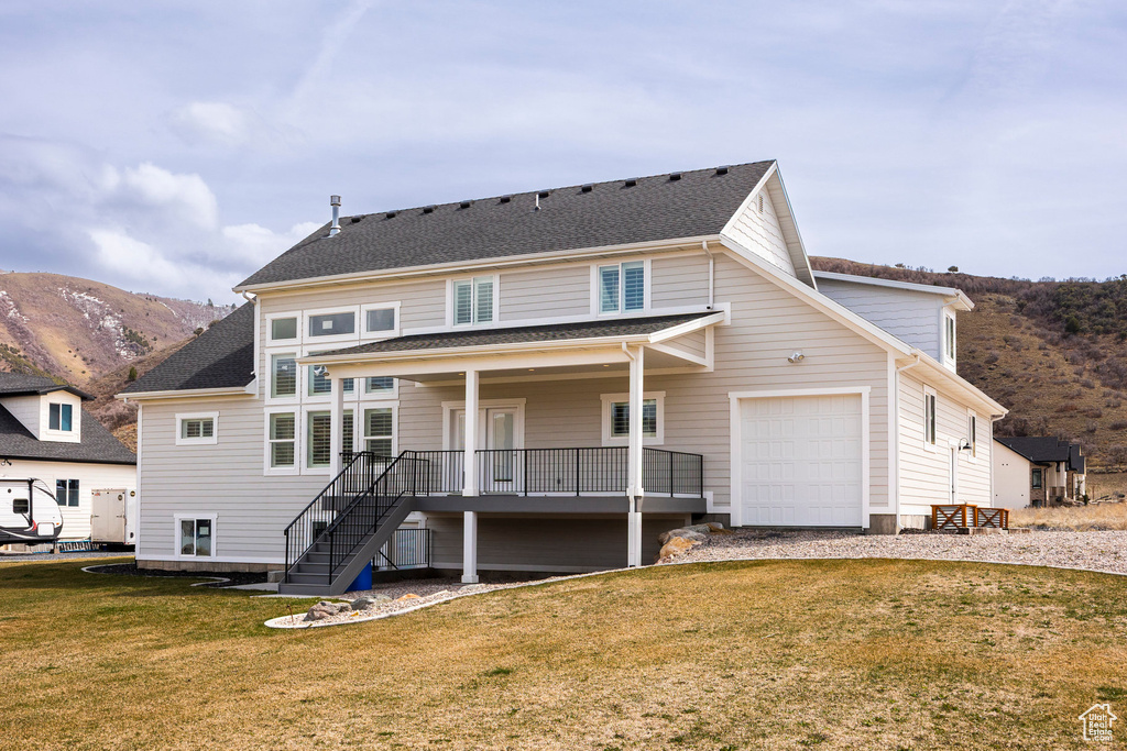 Rear view of property featuring a mountain view, stairway, a yard, an attached garage, and driveway