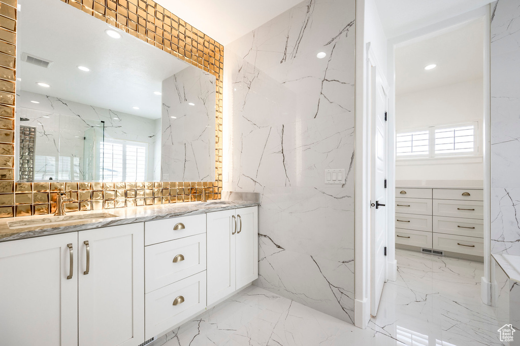 Bathroom featuring stone wall, double vanity, marble tiled floors, a marble finish shower, and recessed lighting