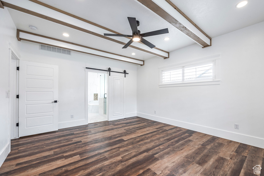 Unfurnished bedroom with beamed ceiling, a barn door, dark wood-style floors, recessed lighting, and ensuite bath