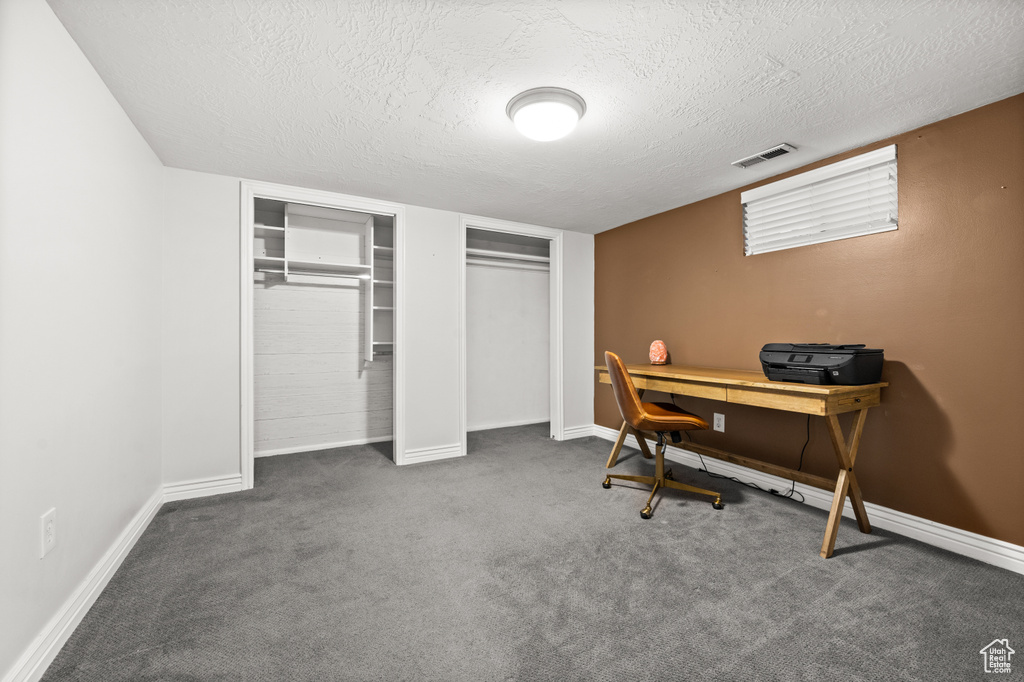 Carpeted office space with a textured ceiling, baseboards, and visible vents