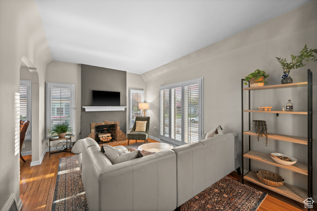 Living room featuring baseboards, a brick fireplace, visible vents, lofted ceiling, and wood finished floors