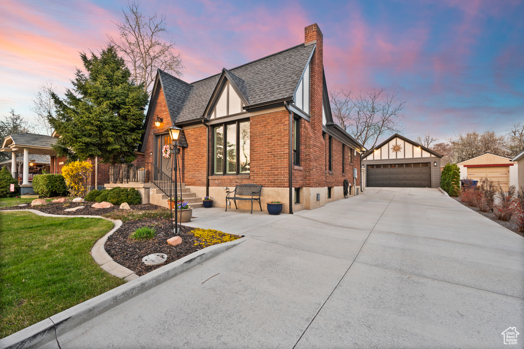 Property exterior at dusk with an outdoor structure, a chimney, brick siding, a garage, and a shingled roof