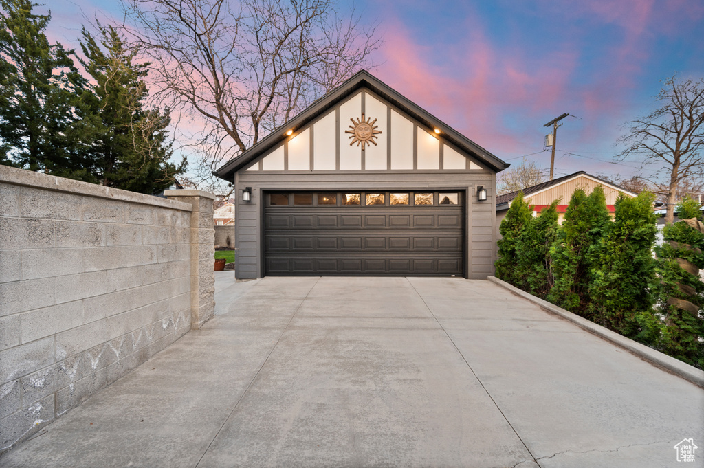 Garage at dusk featuring fence and a detached garage