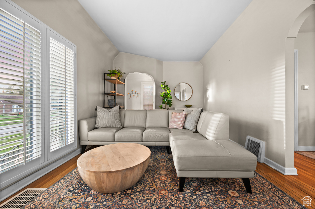 Living room featuring arched walkways, visible vents, wood finished floors, and lofted ceiling