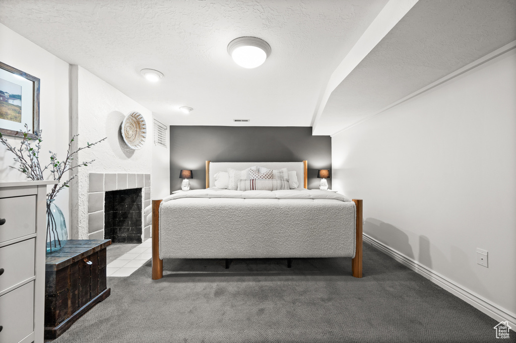 Carpeted bedroom with a textured ceiling, a tiled fireplace, baseboards, and visible vents