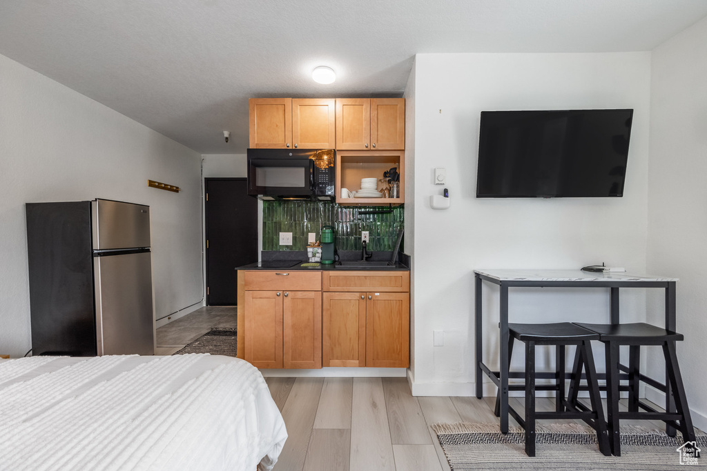Bedroom with baseboards, light wood-type flooring, and freestanding refrigerator