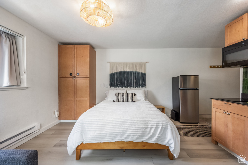 Bedroom featuring light wood finished floors, baseboard heating, and freestanding refrigerator