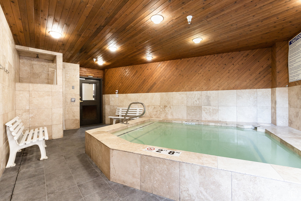 Bathroom with tile patterned floors, tile walls, wooden ceiling, and a garden tub