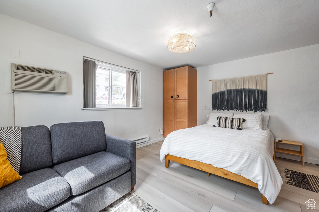 Bedroom featuring light wood-style flooring, a baseboard heating unit, and a wall unit AC