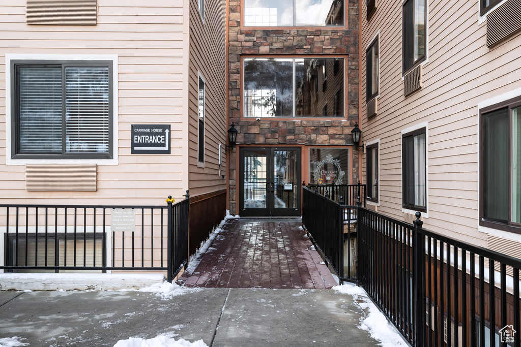 Snow covered property entrance featuring french doors, fence, and stone siding