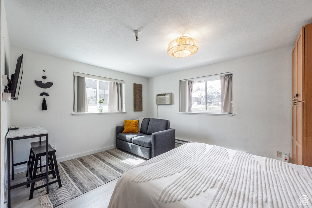 Bedroom with an AC wall unit, baseboards, a textured ceiling, and light wood finished floors