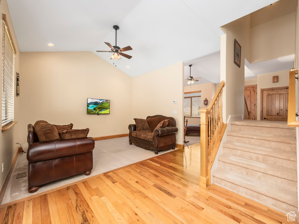 Living area featuring ceiling fan, wood finished floors, stairs, baseboards, and high vaulted ceiling